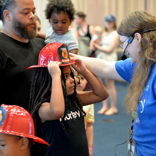 A family stands together as a child puts on a fire hat at an OPL event.
