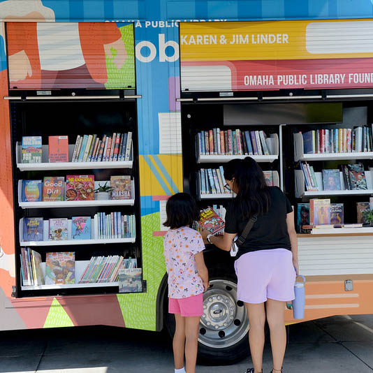 A guardian and child browse books available for checkout on OPL’s mobile library Poppy.