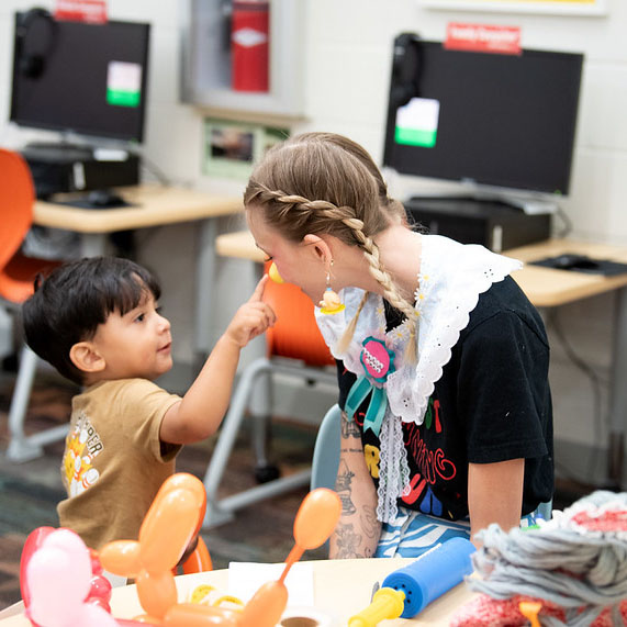 A young child interacts with a balloon artists at A.V. Sorensen's birthday celebration.
