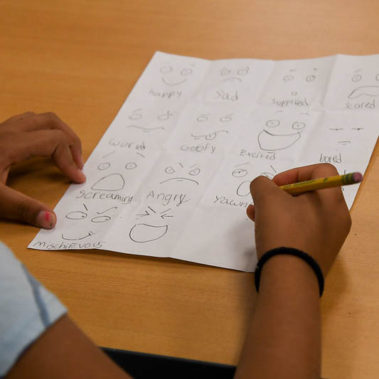 A kid draws different facial emotions on a piece of paper.