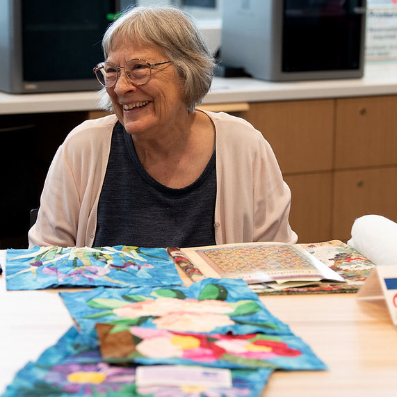 A patron smiles as they sit in front of their crafts they made at an OPL event.